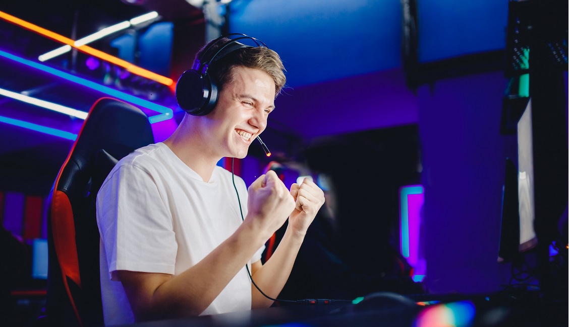 Streamer young man rejoices in victory professional gamer playing online games computer with headphones, neon color.